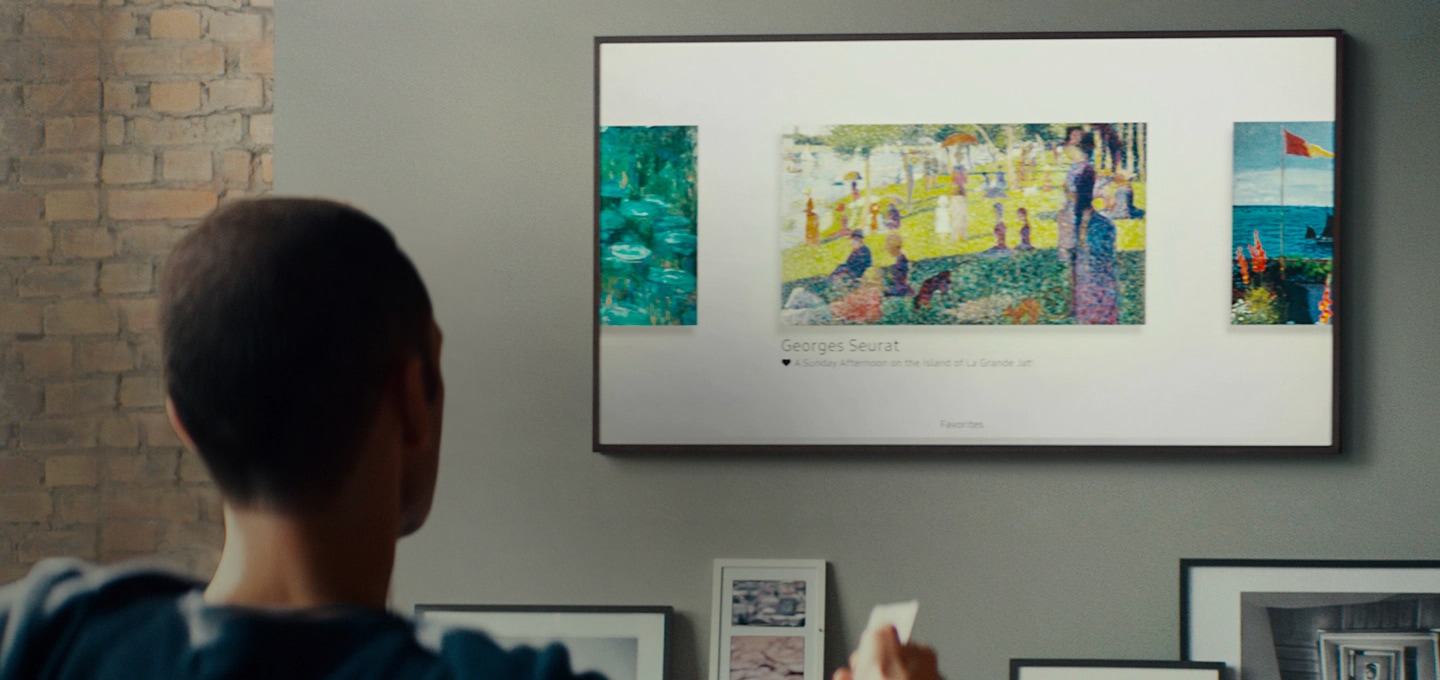 Un homme utilise une télécommande pour chercher des peintures qui sont affichées sur The Frame, qui est accroché au mur dans son salon.