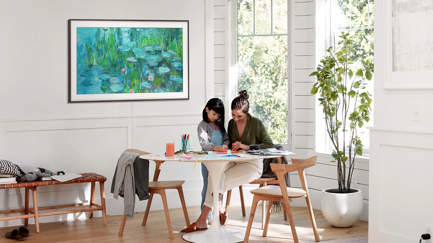 The Frame avec un cadre noir est installé sur un mur de bois blanc dans une cuisine. A l'image, une peinture de Claude Monet de la série Les Nymphéas et au premier plan une mère et sa fille qui dessine sur la table. 